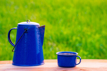 Kettle, blue enamel, and coffee mugs On an old wooden floor, Blurred background of rice fields at...