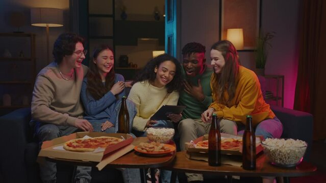 Company sitting by table with pizza while laughing sincerely