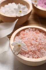 Fototapeta na wymiar Different types of sea salt and flowers on light table, selective focus. Spa products