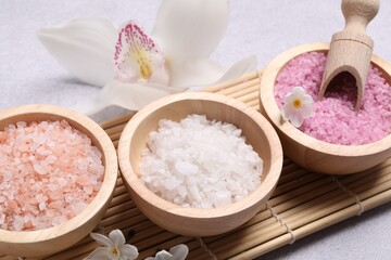 Different types of sea salt and flowers on light table, closeup. Spa products