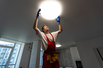 Electrician at work. Service for the repair of electrical wiring and replacement of ceiling lamps. A builder is installing a loft-style wooden ceiling. Rent-a-gent helps with the housework