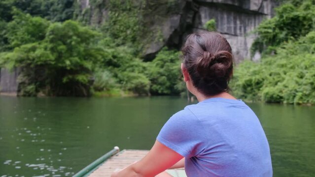 Woman with her back on a boat in Vietnam in Tam Coc exploring the wonders of the area and nature. Solo woman travel adventures in Southeast Asia, discovering new cultures and adventures.