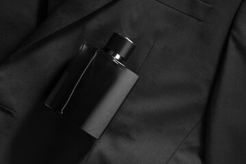 Luxury men's perfume in bottle on black jacket, top view. Space for text
