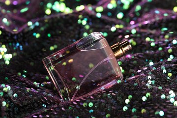 Luxury perfume in bottle on fabric with colorful sequins, closeup