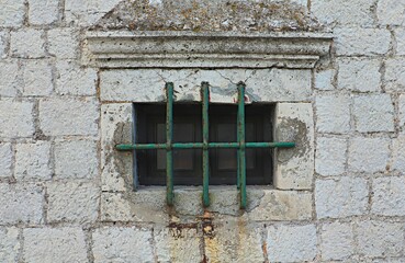window of an old house with a thick iron grille covered with green paint