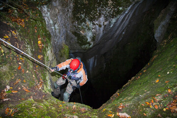  A speleologist man exploring a huge hidden cave hanging on a rope for safety and preparing to go...
