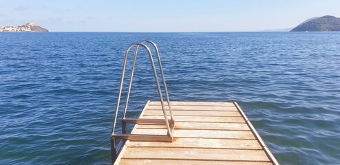 Wooden pier with a railing against the backdrop of the blue sea and the city of Portoferraio.