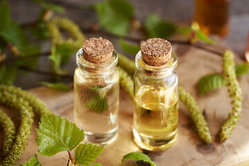 Two transparent bottles of essential oil with birch tree branches with catkins and young leaves in...
