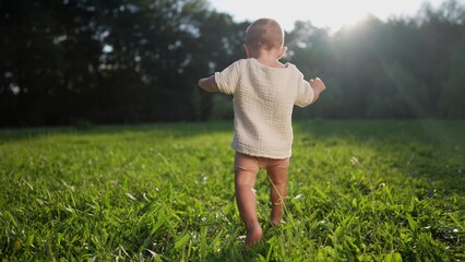 baby takes first steps in the park. happy family kid dream concept. son baby to walk takes the first steps in the park on green grass. baby son taking first steps lifestyle