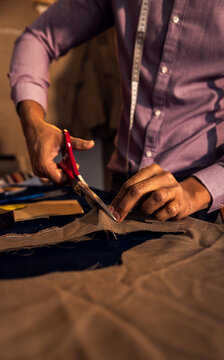 Male fashion tailor working on the suit design in his workshop cutting fabric with scissors.