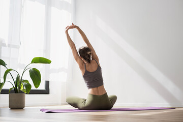 Woman doing fitness exercises at home. Girl training and practicing yoga near floor window in yoga studio. Harmony, balance, meditation, relaxation, healthy lifestyle, mindfulness concept.