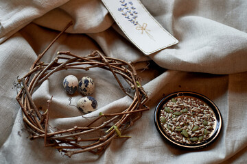 A wreath made of quail eggs beautifully displayed on a wooden serveware, accompanied by a plate of assorted seeds. The arrangement is adorned with twigs and set on a metal tableware