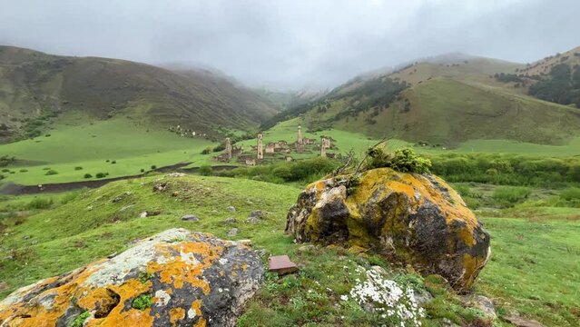 View of the medieval Targim tower complex in the Caucasus mountains surrounded by greenery. The Caucasus Mountains on a cloudy day in Ingushetia. Russia, 4K.
