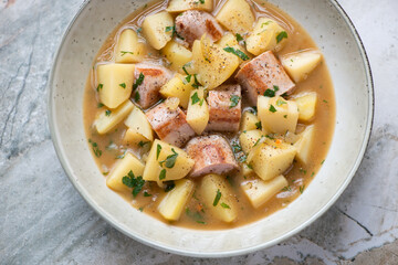 Plate of Dublin coddle or Irish sausage and potato stew, horizontal shot on a grey granite surface, elevated view, middle close-up