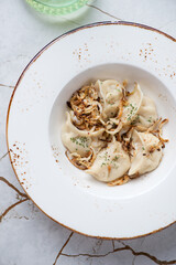 Plate of vareniki dumplings with caramelized onion, vertical shot on a white granite background, flat lay