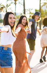 Vertical photo of multiethnic group of young friends running happily together while holding hands. Travel lifestyle concept with multiracial group of millennial tourists having fun in summer 