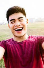 Vertical self-portrait of happy asian young man laughing at city park. Youth people and happiness concept