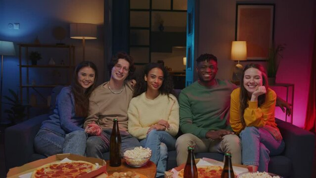 Diverse teenagers sitting on couch and smiling at camera