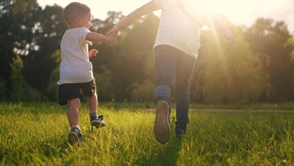 children run in the park. a boy and a girl holding hands run through the grass in the summer at sunset in the park. happy family kid dream concept. children run at sunset in summer hold hands sun