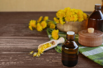 Fresh dandelion flowers and oil in a glass bottle on a wooden table. Flower essential oil. Green...
