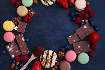 Macarons, chocolate, cookies, berries and various nuts on dark blue background. Top view.
