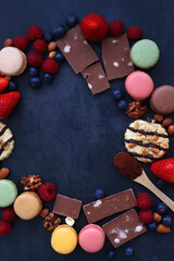 Macarons, chocolate, cookies, berries and various nuts on dark blue background. Top view.