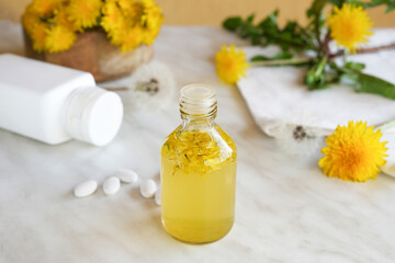 Dandelion tincture or oil bottle, mortar  on a white marble table. Herbal medicine. Side view. 