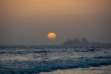 Sunset over the sea with a city in silhouette - 786218167