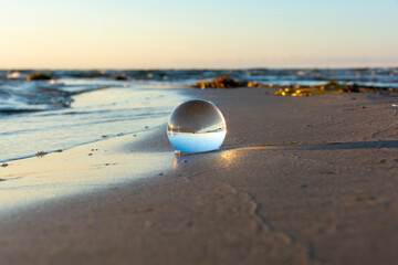 Beach and sea reflected in a sphere lying in the sand in the waves