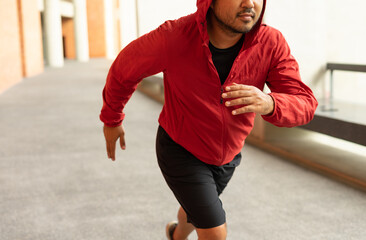 Sportsman wearing a red jacket running on the background of a brick wall stadium. Fitness man...