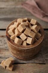 Brown sugar cubes in bowl on wooden table, closeup