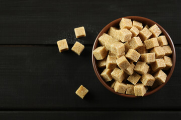 Brown sugar cubes in bowl on black wooden table, top view. Space for text