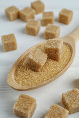 Brown sugar cubes in spoon on white wooden table, closeup