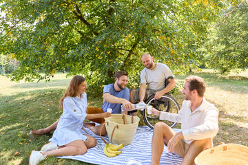 Inclusive outdoor picnic with friends, joyful moment among diverse group in a sunny park