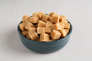 Brown sugar cubes in bowl on light textured table