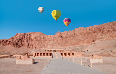 Hot air balloon flying over Hatshepsut Temple at sunrise in Valley of the Kings and red cliffs western bank of Nile river - Luxor- Egypt