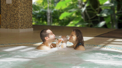 Lovers couple clink glasses while relaxing in the hot tub