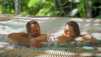 Happy young lovers couple drinking sparkling wine while relaxing in the whirlpool bath hot tub at...