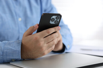 Man using smartphone at table in office, closeup