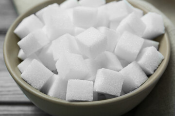 White sugar cubes in bowl on wooden table, closeup