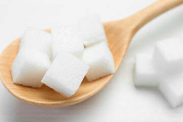 Many sugar cubes and wooden spoon on white table, closeup