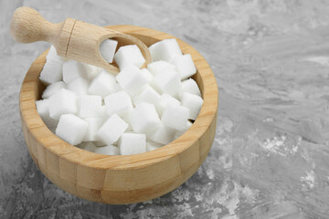 White sugar cubes in wooden bowl and scoop on grey table. Space for text