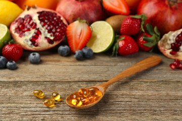 Vitamin pills in spoon and fresh fruits on wooden table