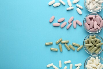 Different vitamin pills on light blue background, flat lay. Space for text