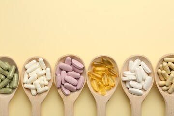 Different vitamin pills in spoons on pale yellow background, flat lay. Space for text