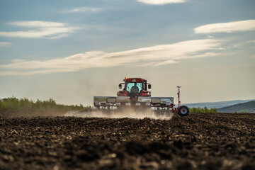 rear view of a working tractor with seeder with dust raising up in ploughed field