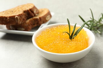 Fresh pike caviar in bowl, bread and rosemary on light grey table, closeup