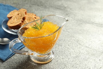 Fresh pike caviar in gravy boat, bread and spoon on grey table, closeup. Space for text