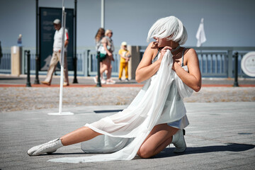 Young sexy girl in space silver micro skirt dancing with white silk scarf waving gracefully, female outdoor dance performance on seaside promenade creating an arousing outdoor spectacle - obrazy, fototapety, plakaty