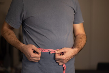 Man excess holding a measuring tape weight abdomen. Measurements before weight loss, first degree obesity, it's time to deal with excess weight, no face, body, mockup, overweight concept - obrazy, fototapety, plakaty
